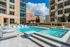 Luxurious urban apartment complex featuring a sparkling outdoor pool with sleek lounges and modern architectural design under a bright blue sky.