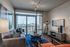 Chic living room with elegant decor, floor-to-ceiling windows showcasing a stunning city view, and modern furniture on a stylish blue rug.