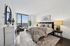 Luxurious bedroom with breathtaking city view, featuring a plush bed, artistic decor, and cozy seating area by floor-to-ceiling windows.