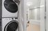 Modern apartment bathroom with sleek design featuring a stackable washer and dryer alongside a pristine bathtub and elegant shelving.