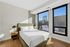 Bright and modern bedroom featuring a cozy bed with soft white linens, elegant side tables, and large windows showcasing a stunning urban view.