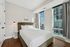 Bright and modern bedroom with plush bed, sleek bedside lamps, and floor-to-ceiling windows offering a stunning city view.