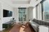 Bright and modern living room with a sleek gray couch, large windows allowing natural light, a wall-mounted TV, and a stylish coffee table on a textured rug.