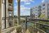 Inviting balcony view from modern apartment overlooking lush greenery and stylish neighboring buildings under a bright blue sky.