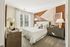 Elegant bedroom with plush bed, modern geometric accent wall, and stylish furnishings accented by natural light from large windows.
