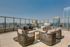 Luxurious rooftop terrace showcasing modern wicker seating, a central fire pit, and panoramic city skyline views.