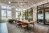Luxurious apartment co-working space featuring modern lighting, a long wooden table with stylish chairs, and large windows offering abundant natural light.