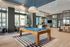 Modern and luxurious recreational lounge with a sleek pool table, stylish seating area, and elegant open-concept dining space, bathed in natural light.