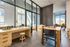 Modern apartment lounge with natural wood furniture, expansive windows, and a cityscape view, creating a bright and inviting space.