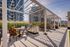 Modern rooftop summer kitchen with elegant seating and stainless steel grill, set against a backdrop of urban high-rises and lush greenery.