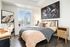 Bright and modern bedroom with a large window view of the city skyline, featuring a cozy bed, stylish decor, and a chic floral artwork.