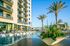 Luxurious apartment building with modern balconies overlooking a stunning pool area, surrounded by tropical palm trees and elegant lounging spaces.