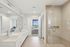Elegant modern bathroom with dual sinks, a spacious glass shower, and a view of a stylish bedroom with cityscape window.
