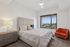Bright, modern bedroom with plush bedding, chic decor, and expansive city views through a large window.