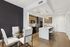 Modern apartment kitchen and dining area featuring sleek wood cabinetry, elegant island with bar stools, and a chic round glass dining table with stylish white chairs.