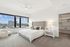 Elegant bedroom with plush carpeting, modern decor, and panoramic city views through expansive windows.