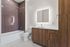 Modern bathroom featuring sleek wood cabinetry, illuminated mirror, and stylish tiled bathtub.