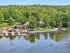 Scenic waterfront area with vibrant greenery, cozy buildings, docks, and neatly arranged canoes and paddle boats under a clear blue sky.