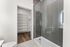 Modern bathroom featuring a sleek glass shower with elegant tiles, opening to a spacious walk-in closet with built-in shelving and warm wood flooring.