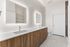 Modern bathroom featuring a double vanity with sleek wooden cabinets, illuminated mirrors, and a spacious layout.