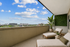 Chic urban balcony with lounge chairs, lush greenery, and stunning city skyline views under a clear blue sky.