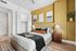 Stylish bedroom with golden accent wall, cozy bed adorned with pillows and throws, modern wooden nightstand, and elegant artwork, perfect for relaxation.