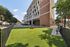Modern outdoor recreation area with lush green artificial turf, comfortable benches, and a playful dog enclosure adjacent to a contemporary brick building, perfect for relaxation and leisure.
