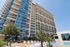 Modern high-rise apartment building with glass facade, lush landscaping, and inviting pool area under a clear blue sky.