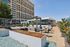Luxurious urban apartment complex with a stylish outdoor lounge area featuring modern seating, vibrant greenery, and a sleek glass building backdrop.