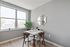 Bright dining area with a modern wooden table set, large window, decorative mirror, and lush greenery for a cozy atmosphere.