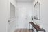 Modern entryway featuring a sleek console table, decorative mirror, and elegant greenery accenting clean white walls.