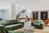 Modern living room with elegant green sofas, stylish open bookshelves, and sleek staircase, offering a warm and inviting ambiance.