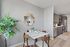 Modern dining area with a chic table set for four, elegant wall mirror, and an open kitchen featuring sleek cabinetry and stainless steel appliances.
