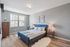 Bright, modern bedroom featuring a cozy blue bed, wooden furniture, and plenty of natural light from a large window.