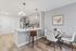 Modern apartment kitchen with sleek gray cabinetry, stainless steel appliances, chic pendant lighting, and an inviting breakfast bar adjacent to a cozy dining area with contemporary artwork.