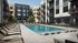 Modern apartment complex with elegant pool area, surrounded by lush greenery and stylish lounge chairs.