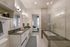 Elegant bathroom featuring double sinks, a sleek glass shower, and a view into a cozy bedroom.