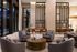 Elegant apartment lobby featuring plush seating around a stylish wooden coffee table, modern decor, and high ceilings with expansive windows.
