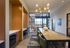 Modern workspace featuring sleek design with wooden accents, a stylish chandelier, and a glass-walled meeting room with vibrant orange chairs.