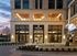 Elegant entrance of a luxury building with modern architectural design, featuring grand glass doors and a striking metallic sculpture at dusk.