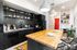 Model kitchen featuring open shelving for crockery, a wash area, a dining table set, and stylish pendant lights hanging overhead.