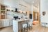 Modern model kitchen featuring a marble island with bar stools, open shelving, and sleek kitchen appliances.