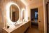 Elegant modern bathroom featuring warm-toned finishes, backlit arched mirrors, a floating double-sink vanity, and marble-look wall tiles.
