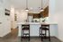 Modern kitchen featuring a white kitchen island, dark wood-finish cabinetry, stainless steel appliances, and dark bar stools