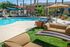 Luxurious outdoor pool area with chic lounge chairs, modern fire pit, and lush greenery under sun sails.