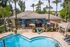 Inviting apartment complex with a sparkling pool, vibrant lounge area, and lush palm trees offering a tropical oasis feel.