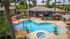 Luxurious apartment complex featuring a stunning resort-style pool with sun loungers and umbrellas, surrounded by lush palm trees and modern architecture.