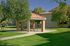 Inviting outdoor gazebo with a picnic table shaded by trees, nestled in a vibrant green lawn, perfect for relaxation and gatherings.