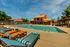 Luxurious outdoor pool area with comfortable loungers and vibrant umbrellas, set against a backdrop of charming terracotta-roofed buildings and lush greenery, perfect for relaxation and leisure.