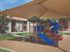 Inviting playground with vibrant slides and covered shade, nestled in a lush apartment community, ideal for family relaxation.